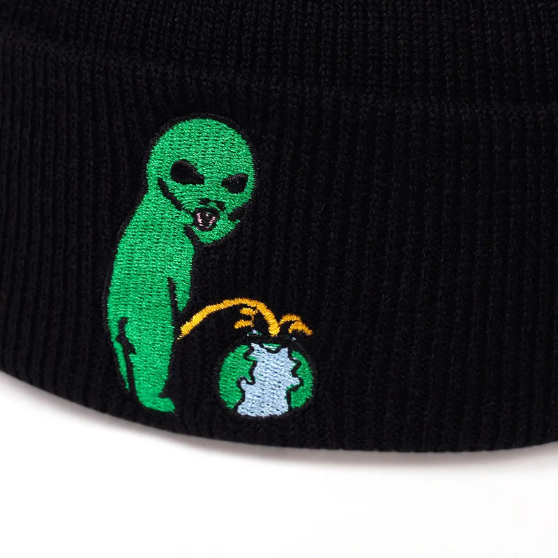 Ribbstickad svart mössa med motiv av en grön alien som urinerar på jorden